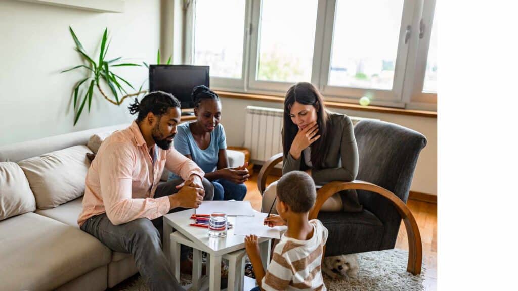 Family therapy and support for people with ADHD - Therapist with a black family providing assistance for a child diagnosed with ADHD. Child is at a table surrounded by family and therapist drawing