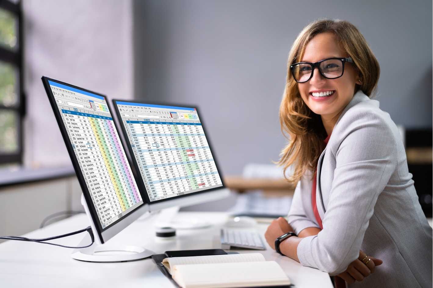 Female Professional Administrative Assistant with white jacket in front of dual computer screens Rowan Center