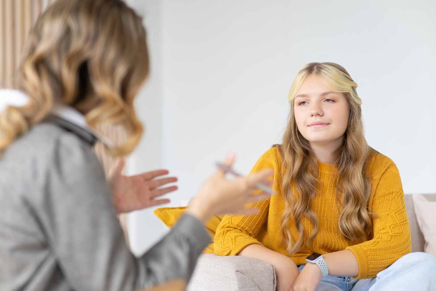 Girl working with a therapist - She's wearing a yellow sweater and therapist in the foreground is blurred