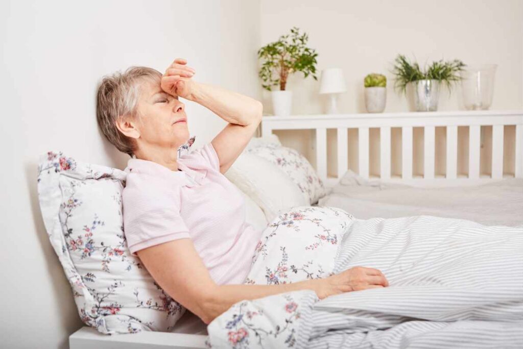 Woman in bed with hand on her head showing the impact of chronic stress on her physical health