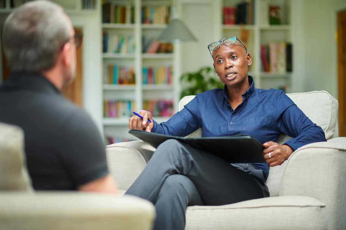 black therapist sitting in a chair with glasses on her head working with white man with a black shirt