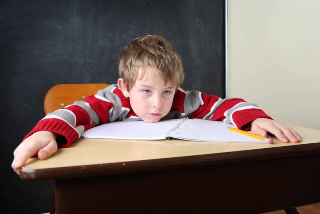 child significantly impacted at school by the inattentiveness of adhd - child with red and gray sweater laying on notebook looking exhausted